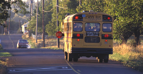school bus coming to a stop with its stop sign extended on the left