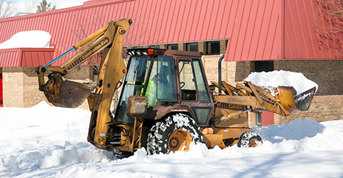 An HCPSS employee uses a backhoe to remove snow from walkways