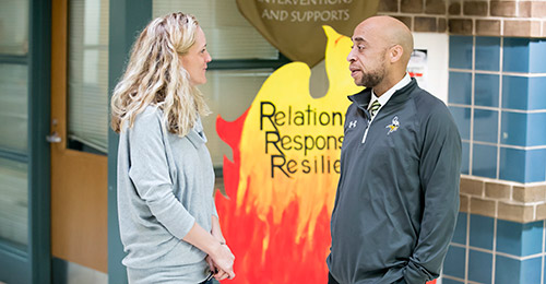 Photo of Anthony Bell talking with another staff member in hallway