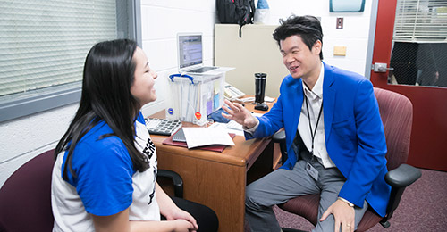 Sung Kim sitting at desk and talking with student