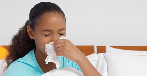 young female in bed blowing her nose into a tissue