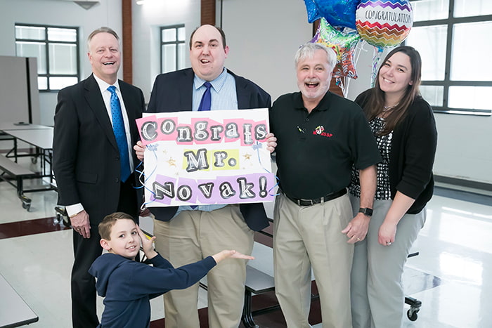 Principal Novak holding up a sign that says 'Congrats Mr. Novak!'