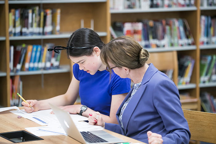 A female student and a teacher look over a document together.