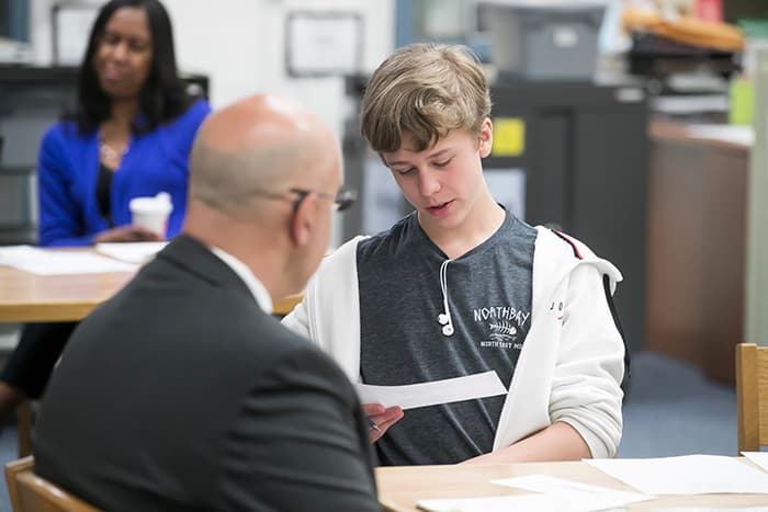 A young male student reads to a teacher.