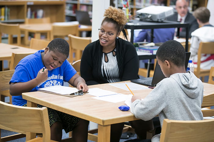 A teacher sits in a library with two students.