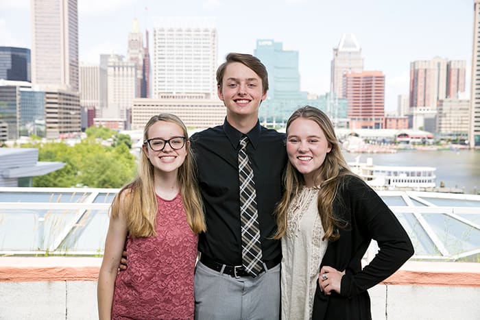 A male and two female students smile with the Baltimore skyline in the background.