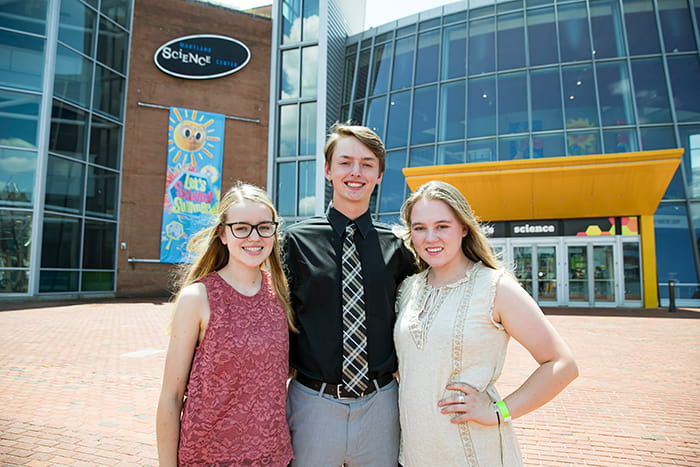 A male and two female students stand outside the Maryland Science Center.