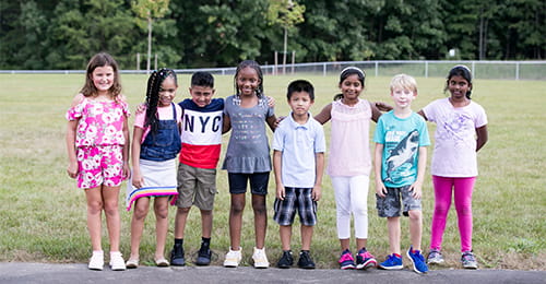 A group of diverse elementary school students arms link together and standing on the blacktop.