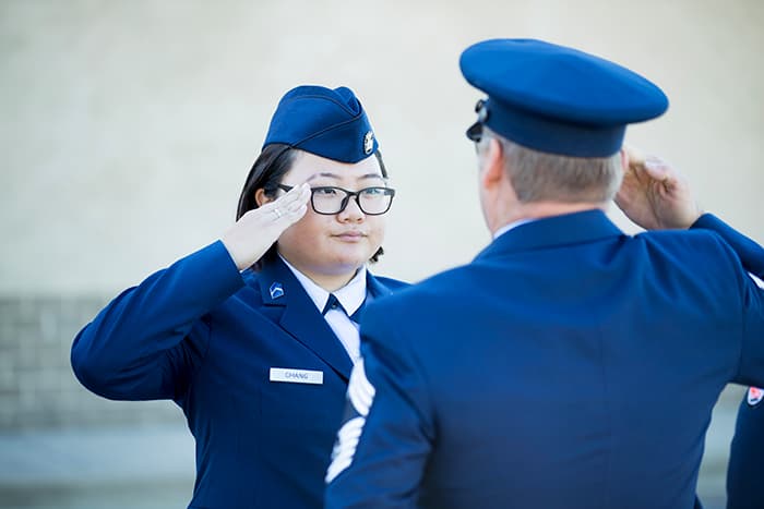 A female student in uniform salutes a uniformed officer.