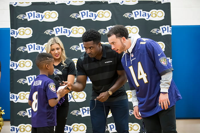 Two Ravens players and a Ravens cheerleader speak with a student.