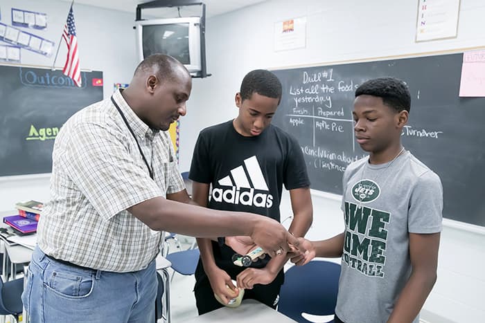 Two African-American PMS students and their teacher hold a model they are working on.