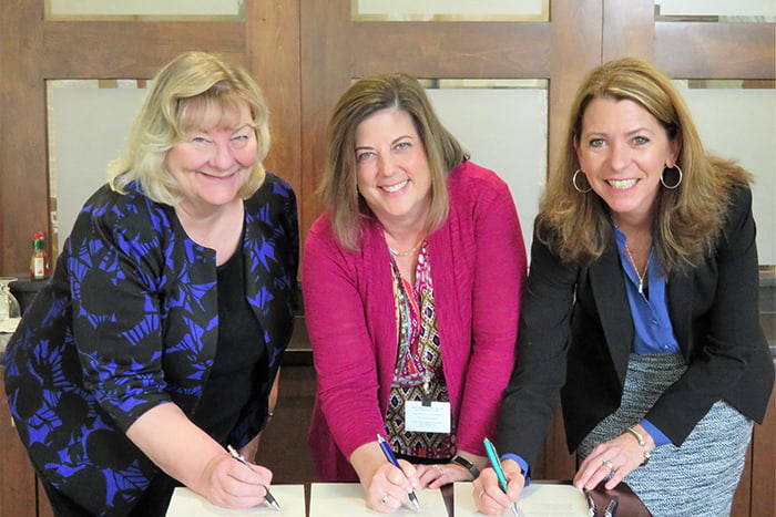 Three women signing a partnership agreement.