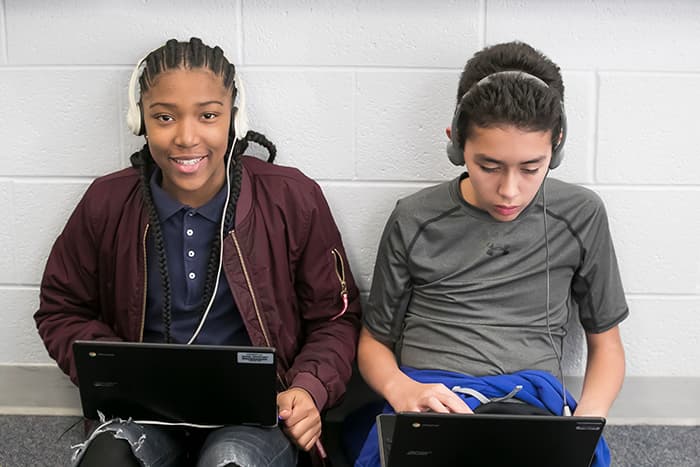 A female and a male students wearing headphones and looking at laptops.