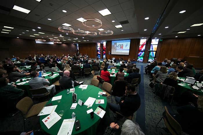 People seated at tables, listening to the State of the Schools.