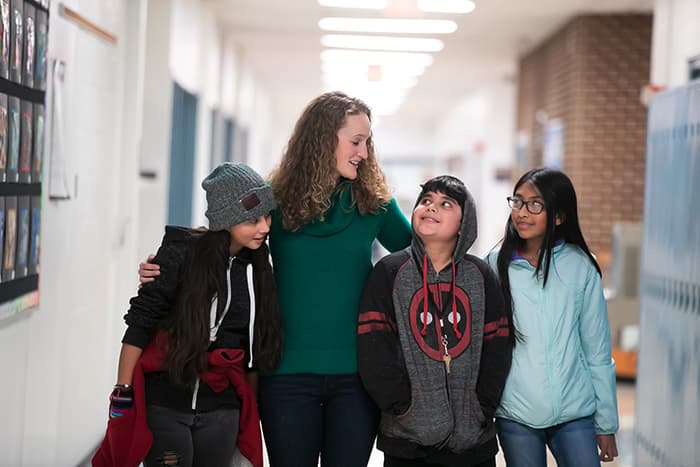 Sarah Mayhew with her arms around a group of students.