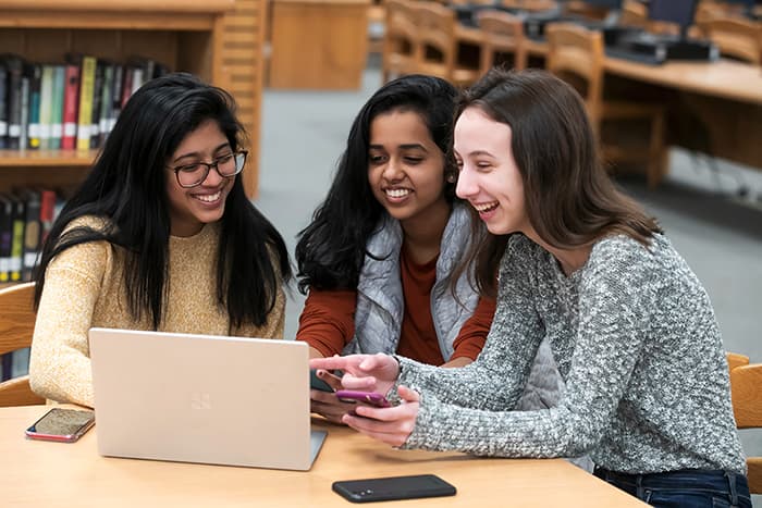 Three teenage girls looking at a laptop in a library.