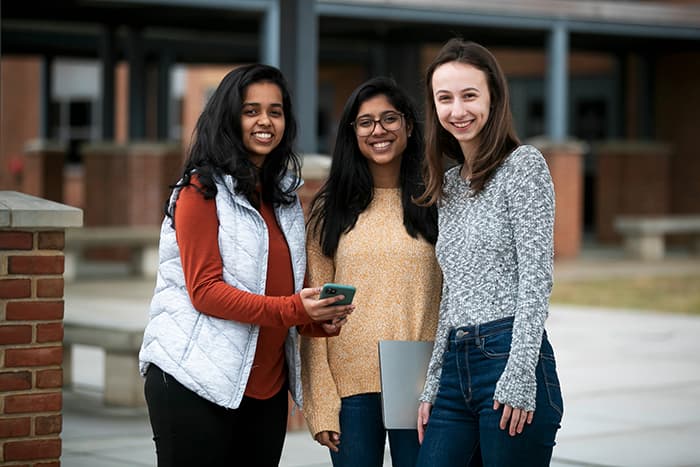Three teenage girls smiling and holding a cell phone.