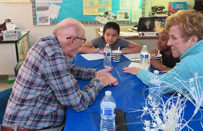 An elderly man and woman speak with two young girls.