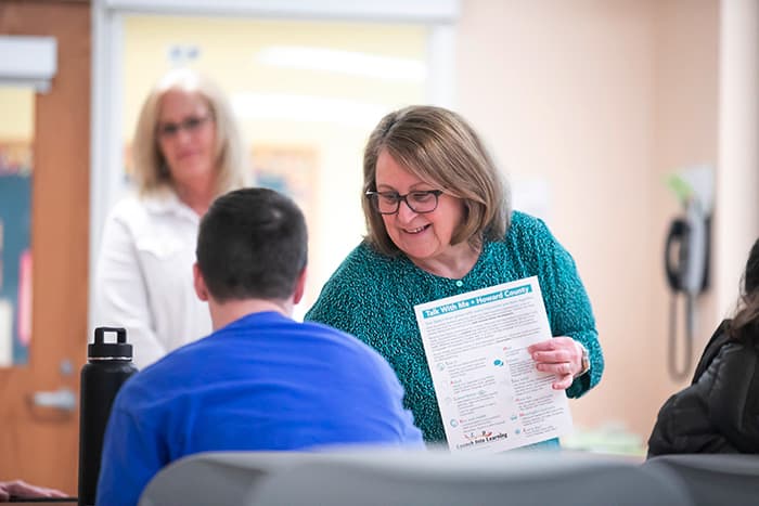 A teacher holds a flyer and talks to a student.