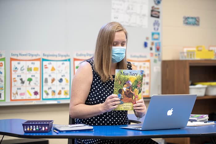 Sara Hancock holding up a book in front of a laptop.