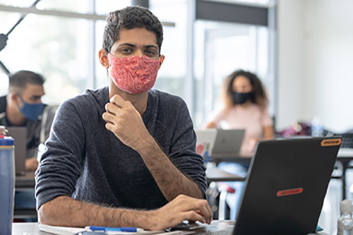 male student wearing face mask at computer in class