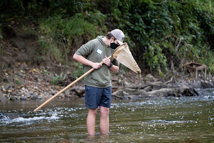 Male student examining a net while standing in stream.