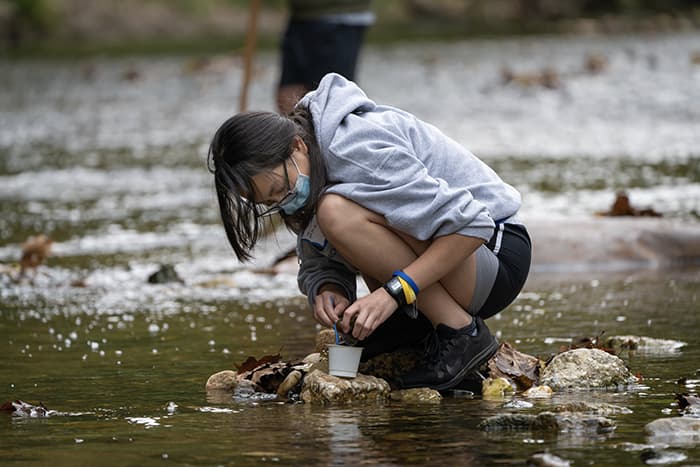 Female student standing in a stream taking a water sample.