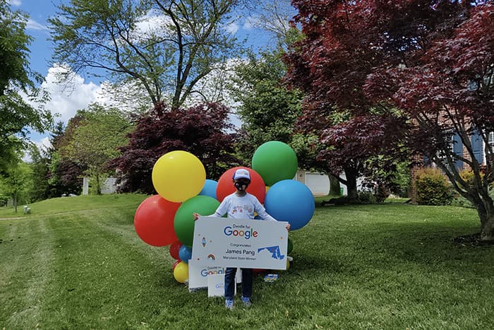 James Pang holding a sign and surrounded by balloons.