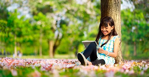 A young girl reading under a tree.