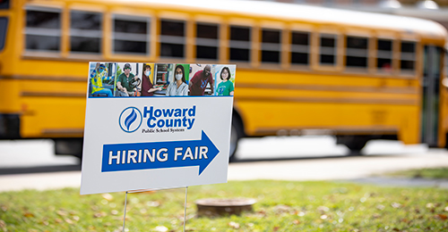 blurred bus in background. HCPSS Hiring Fair sign in foreground