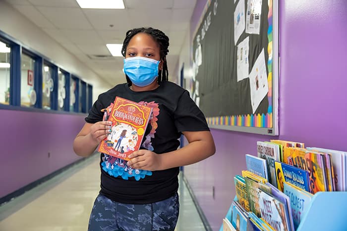 Female student at Running Brook Elementary School reviews a book from the Always Reading book collection.