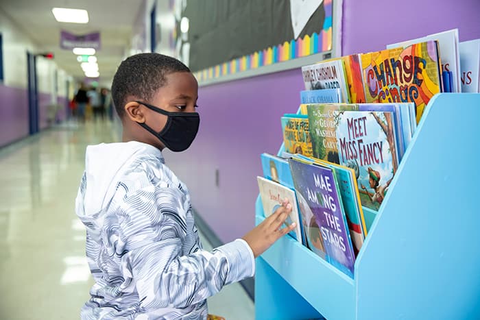 Male student reviewing Always Reading bookshelf at Running Brook Elementary School.