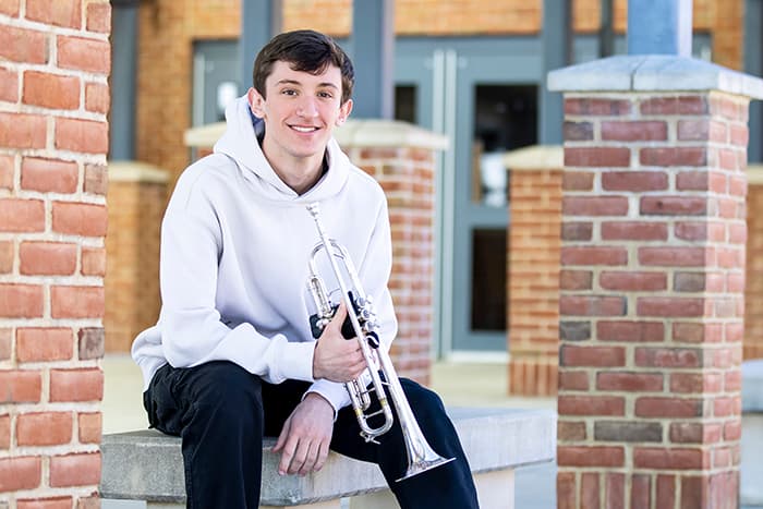 Aiden Interrante sits outside Mt. Hebron High School and holds his trumpet..