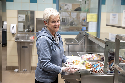 cafeteria worker prepares lunch tray for students