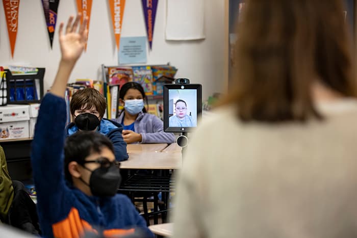 EMMS students in a classroom with their classmate Dylan, who uses a robot to participate.