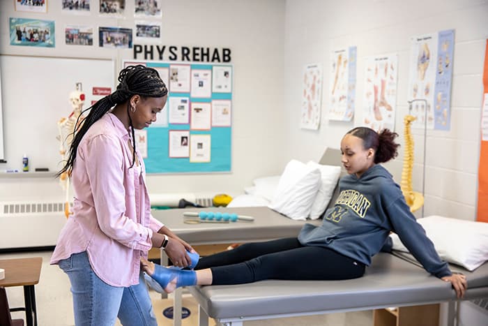 Physical rehabilitation student Mia Swaby-Rowe tapes her peer's ankle.