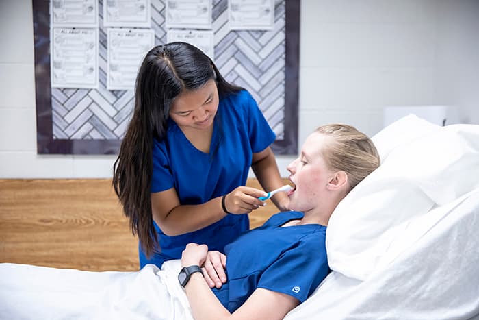 CNA student Kelly Song brushes a female patient's teeth.