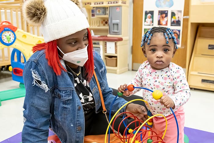 WLHS student sits on the floor while her toddler-aged daughter holds onto a toy.