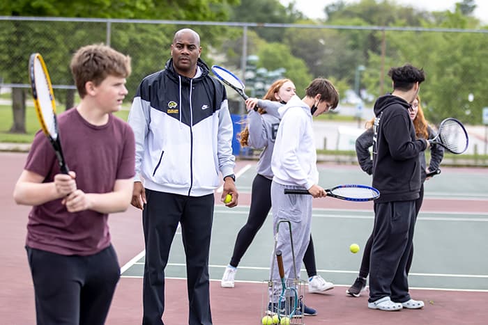 Deon Wingfield watches as his student practices hitting a tennis ball.