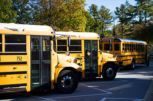 three school buses lined up outside of a school for pickup.