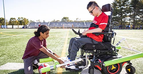 Amitav Kohl making adjustments to Ryan Kobylski's wheelchair device.