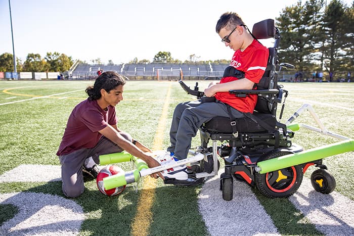 Amitav Kohl making adjustments to Ryan Kobylski's wheelchair device.