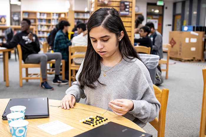 A female MHHS student creates a color-coded bracelet of her name using binary code.