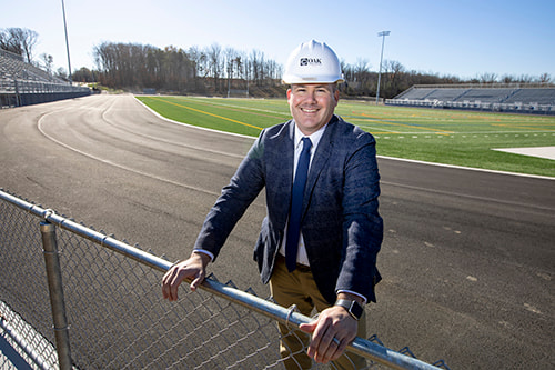 Principal Wasilewski wearing a hard hat and standing in front of the track and football field.