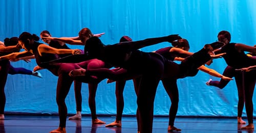 Students in All-County Dance Ensemble lean forward in a pose on stage.
