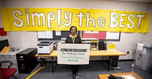 Dr. Chandra McKnight-Dean with 'simply the best' sign behind her.