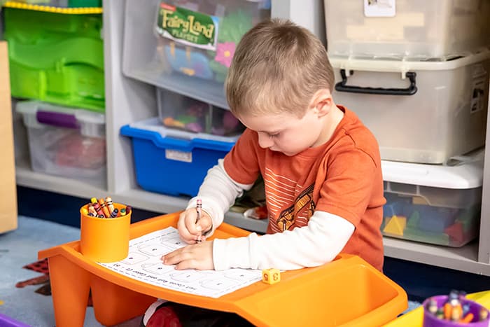 Male pre-k student writing with a crayon.