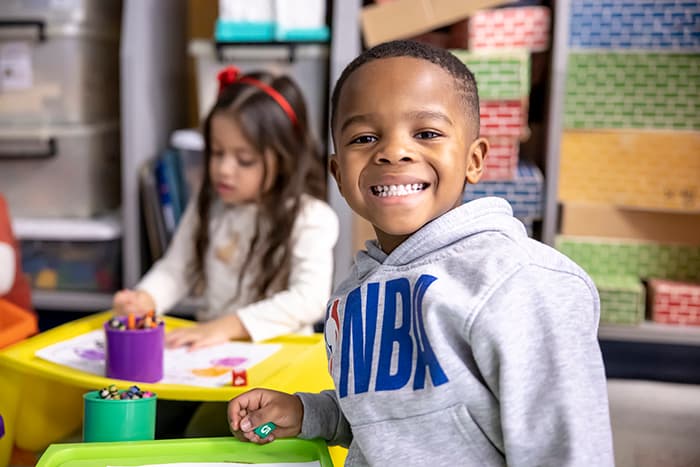 Male Laurel Woods ES pre-k student sitting at a table smiling.