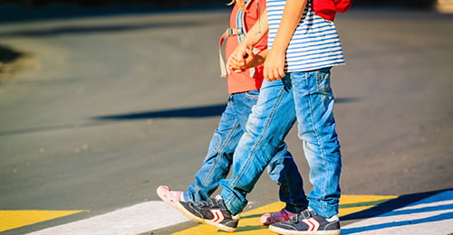 two children holding hands walking through street crosswalk