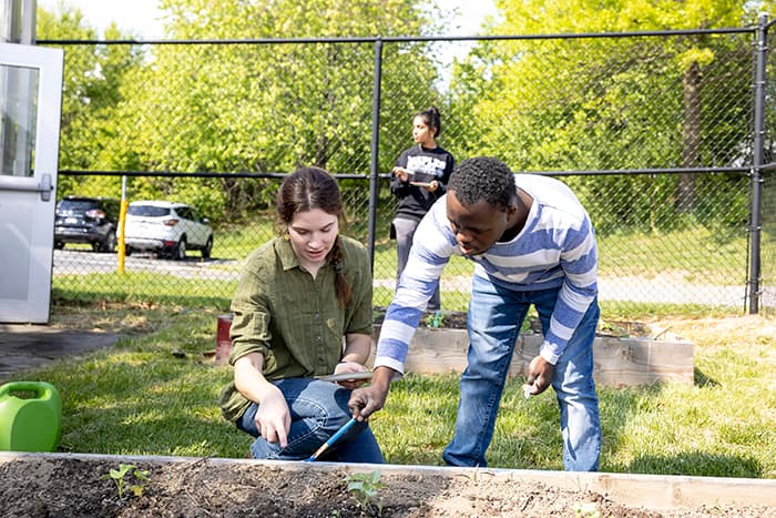 A teacher showing a student how to dig in ths soil.